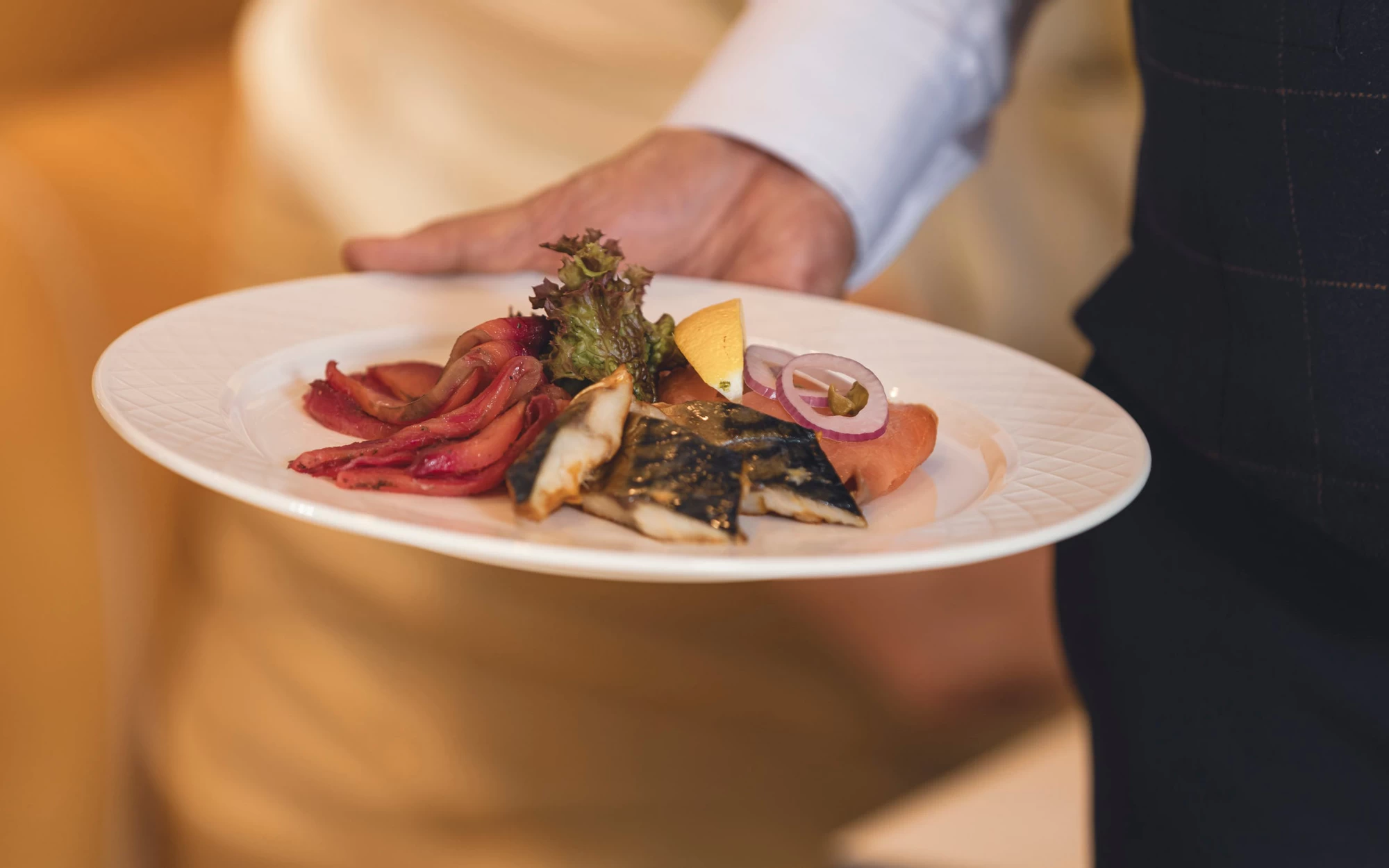 Saga cruise fine-dining photography — plated fish course of mackerel and smoked salmon held by a waiter